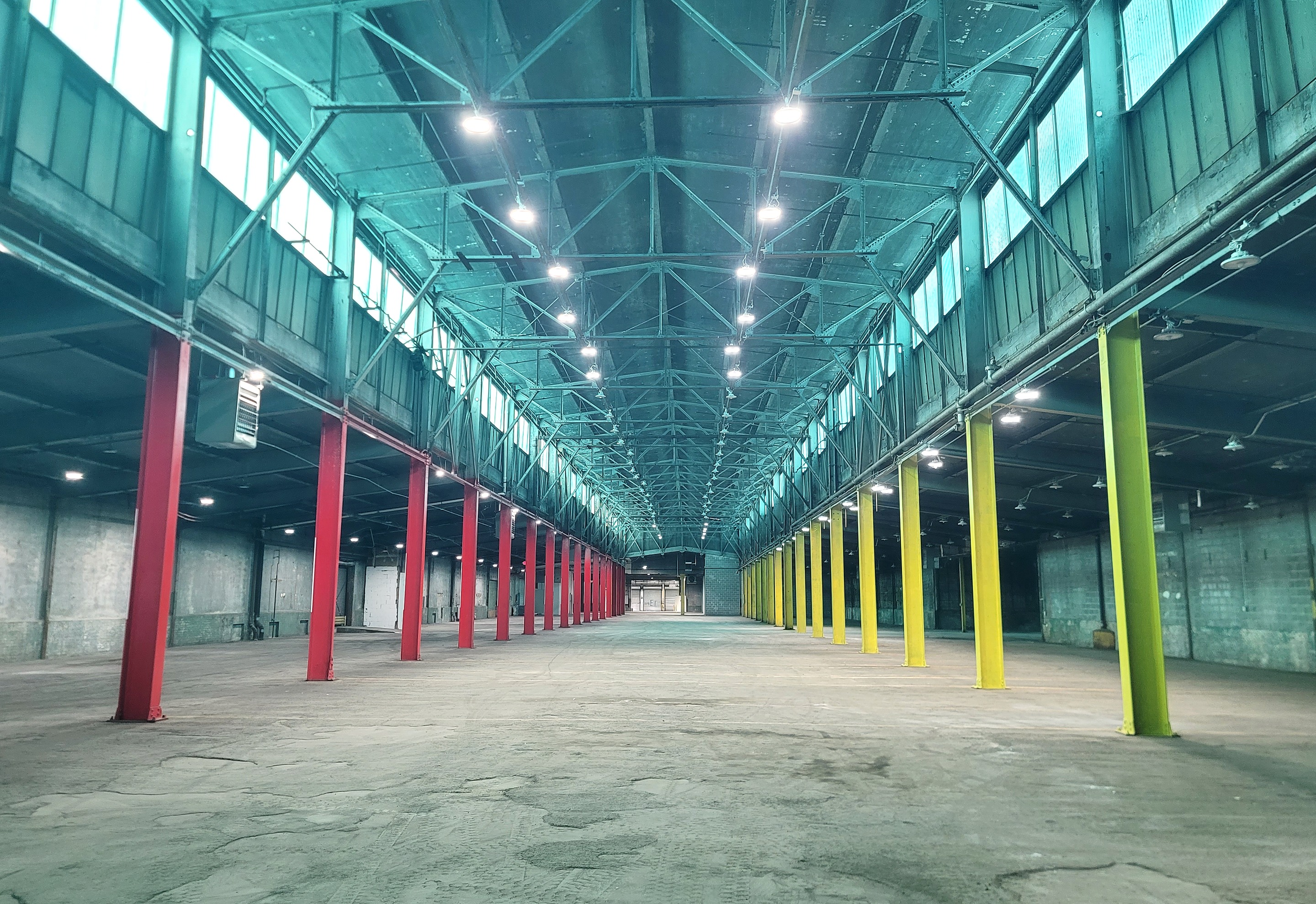 A vast empty mill floor with teal clerestory windows and red, yellow and green columns